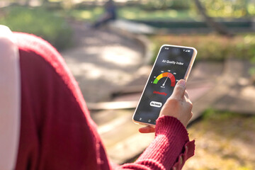 A woman checking the outdoor air quality index using an app on her smartphone. Selective focus.