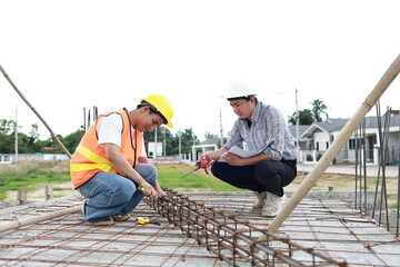 Engineers and architects wearing hardhats collaborate at a construction site, examining blueprints...