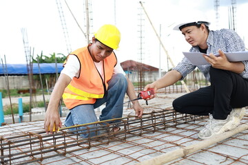 Engineers and architects wearing hardhats collaborate at a construction site, examining blueprints...