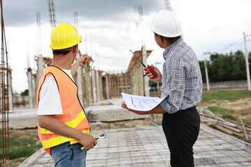 Engineers and architects wearing hardhats collaborate at a construction site, examining blueprints...