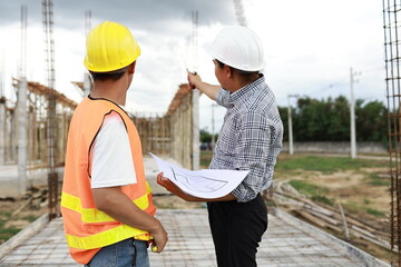 Engineers and architects wearing hardhats collaborate at a construction site, examining blueprints...
