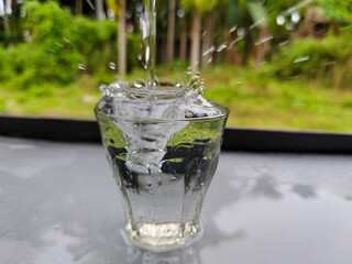 splash of water in a small glass on a table with a green forest background
