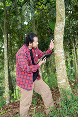 Young researcher conservationist man monitoring rainforest trees with modern gadget, sustainability in action
