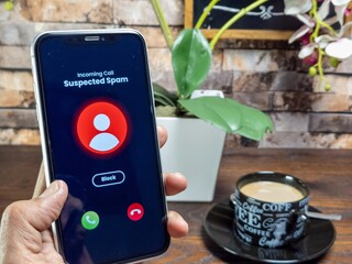 Smartphone displaying incoming spam call with coffee and plant in the background