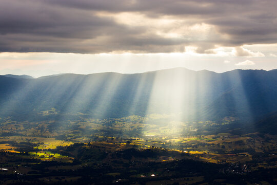 Sun beams and view over the Tweed Valley, Border Ranges mountains  and rural green farmland during a sunset from Mount Warning in New South Wales, Australia