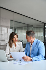 Finance manager and investor discussing corporate project at meeting. Two busy mature professionals man and woman business leaders checking document talking working on laptop in office. Vertical.