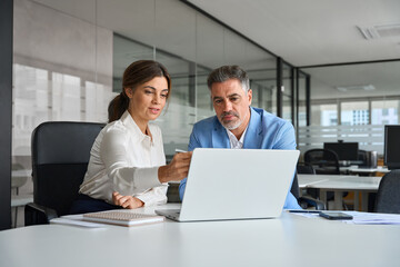 Professional bank manager consulting financial corporate client using laptop. Two busy professional executives team business people of middle age working together on computer at office meeting.