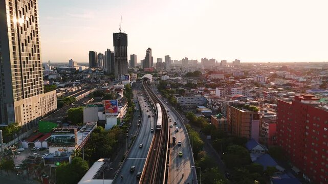 Follow motion track of BTS Skytrain moving above the road toward a station in Thon Buri Bangkok district. Cinematic sunset light and urban landscape