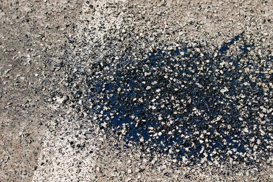 Asphalt patchwork and resin coat applied with gravel and bitumen during road repair works, detailed surface maintenance to fix cracks and prevent further deterioration
