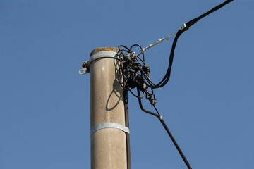 A tangled mess of various wires and cables is seen on a telecom pole situated beneath a bright and...