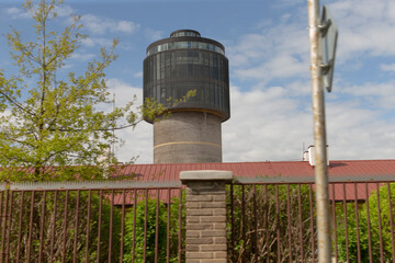 A modern water tower stands in an urban area, surrounded by thriving green plants flourishing...