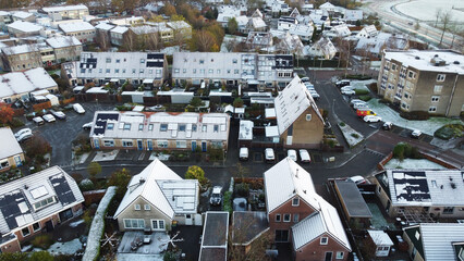 Houses with solar panels snow on roof during winter. Drone shot of street in a residential area neighborhood in The Netherlands.