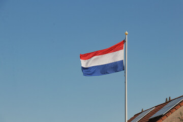 Dutch flag on white pole. Garden rooftop national flagging at home. House in neighborhood.