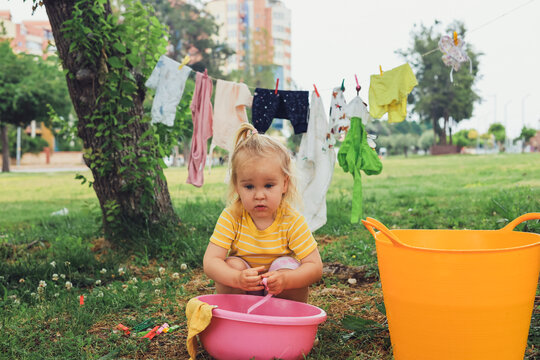 Child and water buckets in park, clothes drying on line