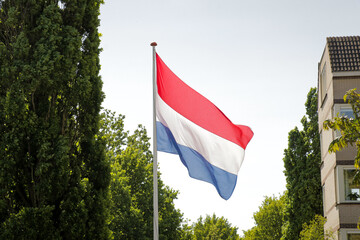 Flag Dutch pole blue sky. Red white blue stripes surrounded by nature trees green neighborhood.. 