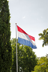Flag Dutch pole blue sky in garden. Red white blue stripes surrounded by nature trees green neighborhood.. 