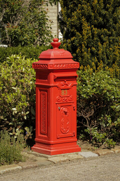 Red English postbox garden driveway. British UK postage post mail letter package delivery.