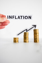 hand holding inflation text in front of growing stacks of coins with arrow going up in the background