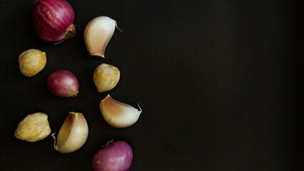 Garlic cloves, shallots and candlenuts arranged on a dark background