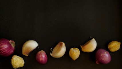 Garlic cloves, shallots and candlenuts arranged on a dark background