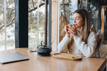 Young Woman Enjoying Tea in Cozy Cafe with Laptop and Smartphone Nearby