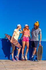 Obraz premium Group of young skaters chatting and enjoying sunny day by blue wall