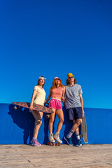 Group of young skaters posing with their skateboards and roller skates against blue wall