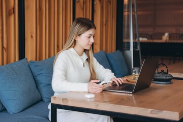 Young woman working remotely using laptop and smartphone in cafe