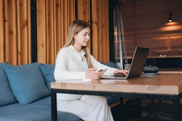 Young woman working on laptop and holding smartphone in cafe