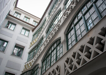 A white stucco courtyard with geometric balcony railings and green-trimmed windows showcases a...