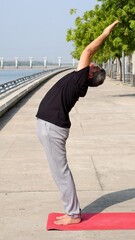 Senior Indian man performing Hasta Uttanasana (Raised Arms Pose) during morning yoga session on a...