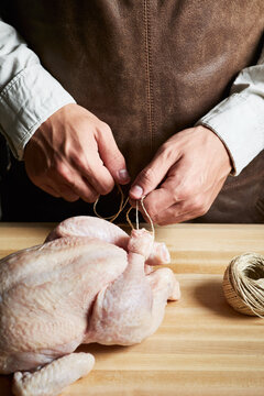 Butcher tying raw chicken on wooden table