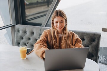 Young woman working on laptop in cafe, drinking orange juice