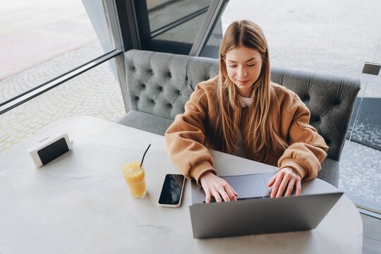 Young Freelancer Woman Working on Laptop in Cafe with Orange Juice