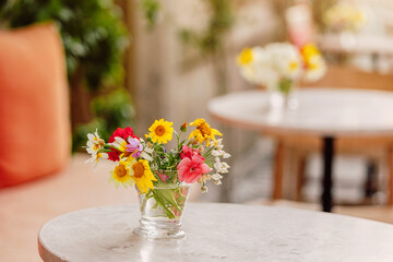 Small glass vase containing a colorful bouquet of wildflowers decorating a table in a restaurant...