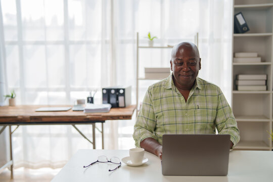 Smiling African American businessman working remotely in a cozy home office, using a laptop while enjoying a cup of coffee, radiating confidence and productivity throughout the day - Powered by Adobe