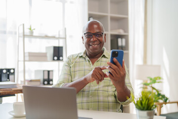 Cheerful african american businessman using mobile phone while working at desk in modern office, browsing internet or checking email on smartphone