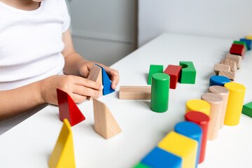 Child engages with colorful wooden geometric blocks on white surface