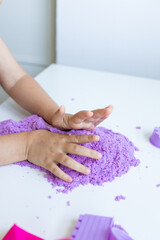Child playing with purple kinetic sand on white table