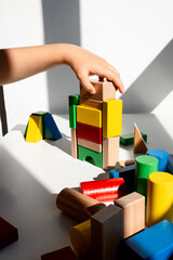 Child hand building colorful wooden block tower in sunlit room