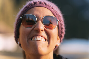 Woman wearing sunglasses and knit hat biting her lower lip in bright sunlight