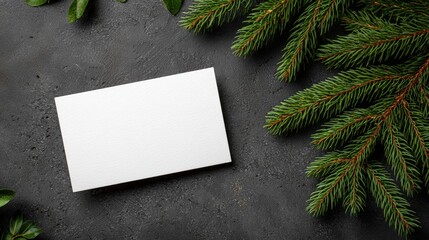 Close-up of a white card on a wooden table decorated with green pine branches, winter holiday theme.