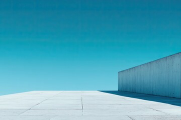 A vast, empty concrete plaza stretches towards a tall, white wall against a bright blue sky