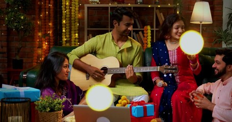 Friends singing during Diwali celebration, Indian Asian young married couple hosting friends with guitar and music in traditional festive wear enjoying Deepavali night at decorated home with sweets - Powered by Adobe