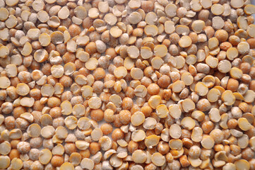 Close-up view of dry split yellow peas scattered in a dense layer. The legumes have a powdery...