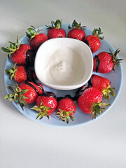 Fresh strawberries arranged on a plate with chocolate drizzle and a bowl of cream in the center. Delicious summer dessert on white background, top view.

