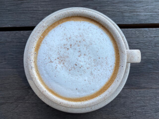 Hot cappuccino coffee in white cup on wooden table background. Art of milk foam circle shape with copy space on brown melt coffee top view