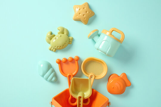 Colorful plastic beach toys falling from bucket on blue background