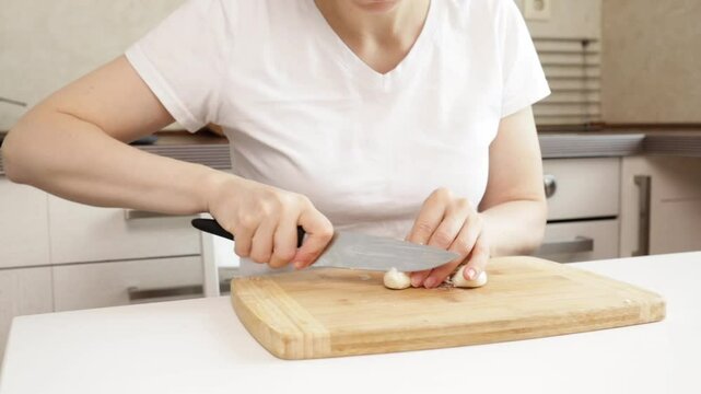 Woman cutting garlic in the kitchen, adult preparing ingredients, domestic food preparation activity.
