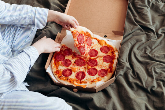 Woman enjoying pepperoni pizza in a cozy bed setting